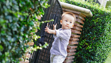 Kid holding a lock and forge gate fence in garden, looking away at something