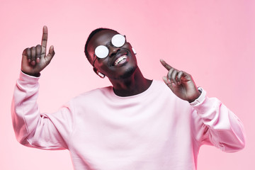 Young smiling african american man listening to music with earphones, dancing isolated on pink...