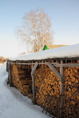 Stack of chopped firewood under the shed shelter on the background of tree - farming, cottage, wintering