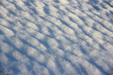 Diagonal wavy texture of blue snow under the sun - winter background