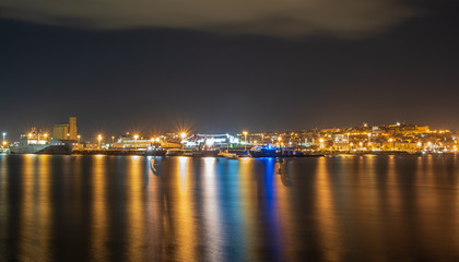 Obraz premium Cityscape of the Mediterranean port of Cagliari seen from the sea. Port of Cagliari during a night full of clouds.