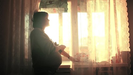 Pregnant woman smiles, rolls up sleeves and opens up curtain on bright kitchen window. Slow motion, 4K UHD.