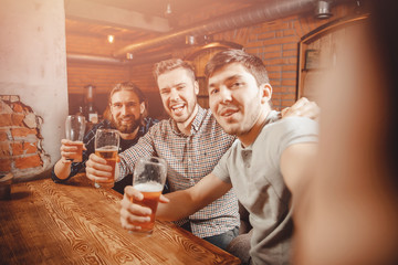 Cheerful friends make selfie photos and drink draft beer at pub bar. Friendship concept