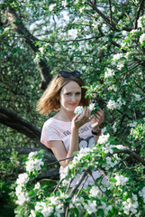 Naklejka na ściany i meble Young beautiful girl stays near an apple tree with wreath made of flowers of apple tree