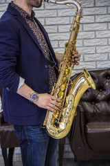 men's hands holding a saxophone against a white wall and a leather sofa