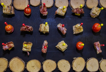 Skewers with food bread bacon and tomatoes on black background with wooden log cabins
