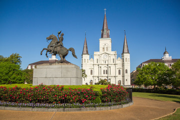 St. Louis Cathedral, Jackson Square, Louisiana, United States. Color horizontal image with Andrew Jackson statue in foreground on left with red flowers. - Powered by Adobe