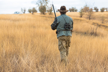 Fototapeta premium Hunter with a hat and a gun in search of prey in the steppe 