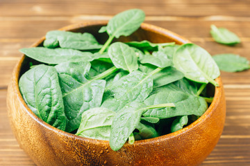 Fresh baby spinach in a wooden bowl on rustic wooden background