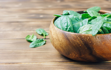 Fresh baby spinach in a wooden bowl on rustic wooden background