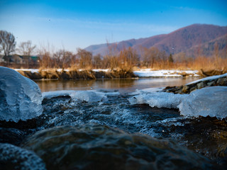 Glades of ice on the banks of a river with a background of mountains