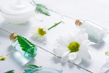 spa setting with cosmetic cream, gel, bath salt and fern leaves on white wooden table background