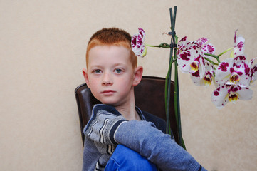 a young preteen boy sits on a chair with flowers