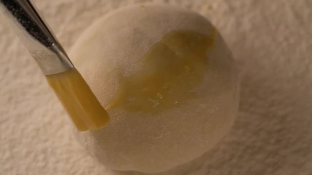 Hand with a brush lubricates dough pie cake with melange on board filled with flour slow motion close up macro shot top view food cooking video