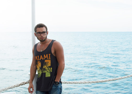 Attractive young sports man standing on a pier by the sea wearing a tank top