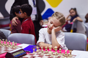 Small cute girl infront of chess board on chess tournament look very bored
