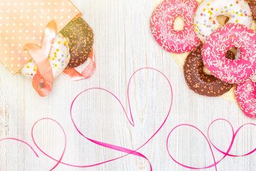 Donuts, gift bag with donuts inside and red ribbon heart on wooden table. Flat lay. Valentine's Day celebration concept