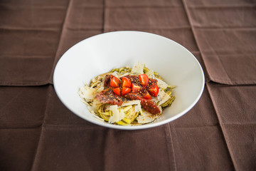Close up of a bow of fresh artichokes salad with red tomatoes cherry and parmesan cheese