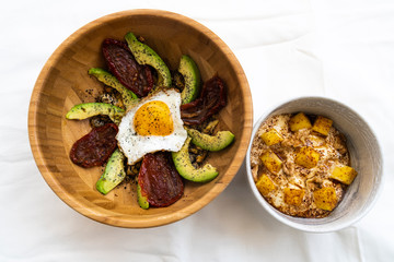 Healthy meal made of egg over avocado slices and dry tomatos and a bowl of yogurt, mango, chestnuts and coffee powder as dessert
