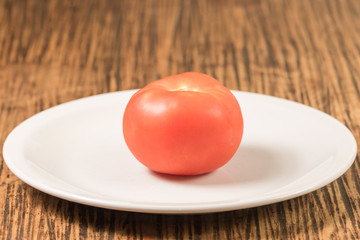shot of whole red tomato on white plate