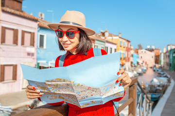 Young female traveler with hat looking at the map on the bridge on Burano island, Venice