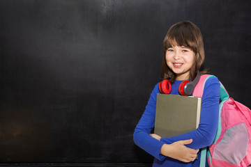 Back to school concept. Happy schoolgirl with backpack and books at the black chalkboard in classroom