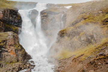 Fresh clean small waterfall  in Iceland in  summer with loads of water flowing between rocks, snow in the background, film effect wih grain