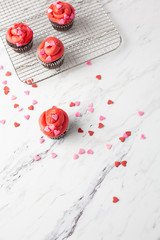 Chocolate Valentine Cupcake with Red Icing and Heart-Shaped Sprinkles on a Wire Cooling Rack; One Cupcake Isolated in Front; Heart-shaped Sprinkles on Countertop
