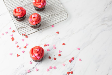 Chocolate Valentine Cupcake with Red Icing and Heart-Shaped Sprinkles on a Wire Cooling Rack; One Cupcake Isolated in Front; Heart-shaped Sprinkles on Countertop