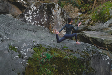 Young slim woman practicing yoga outdoors on big moss rock. Unity with nature concept. Girl stretching ham