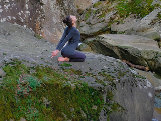 Naklejka na ściany i meble Young slim woman practicing yoga outdoors on big moss rock. Unity with nature concept. Girl sitting back bend