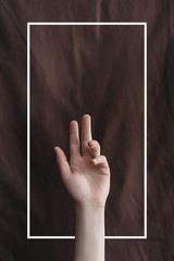 Female hand on the background of brown fabric with a drawn white frame. Minimal creative abstract concept