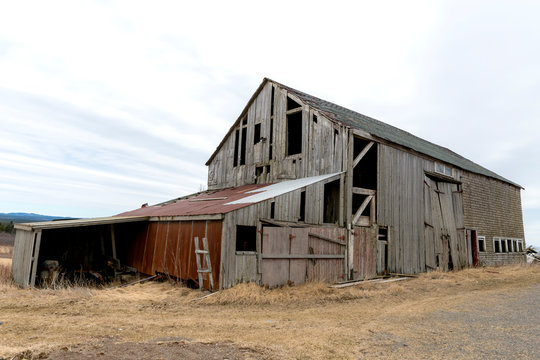 An old abandoned barn. There are holes and missing pieces in the walls. Overcast sky.
