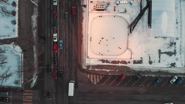 Public ice rink with scating people in city near asphalt road with cars, top aerial view