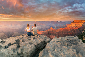 Man and woman sit on the edge of the rim having great conversation during the Grand Canyon sunset