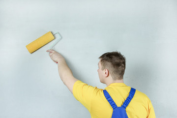 A man treats a wall with a primer using a roller. Worker makes repair. Light photo.