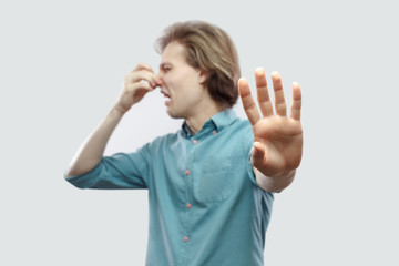 Portrait of rejecting handsome long haired blonde young man in blue shirt standing pinching his...