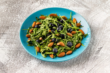 Closeup plate of fresh vegetables vegetarian healthy salad with aragula, nuts, blueberry isolated at stone table background.
