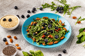Closeup plate of fresh vegetables vegetarian healthy salad with aragula, nuts, blueberry at stone table background.