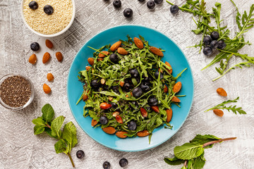Flatlay top view plate of fresh vegetables vegetarian healthy salad with aragula, nuts, blueberry at stone table background.