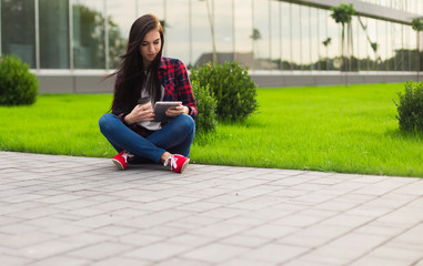 young brunette womanwith tablet serfing in internet on grass