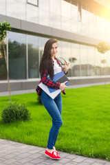 Student Teen Girl in Casual Outfit, Holding Books and Smiling at the Camera While Standing at the Outdoor Walkway.