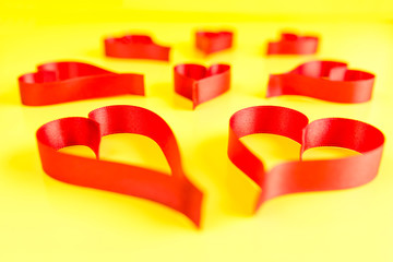 Hearts made from red, satin ribbon on yellow background. Valentines Day concept.