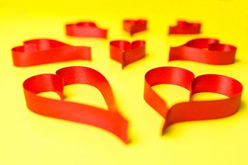 Hearts made from red, satin ribbon on yellow background. Valentines Day concept.