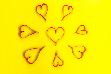 Hearts made from red, satin ribbon on yellow background, view from the top. Valentines Day concept.