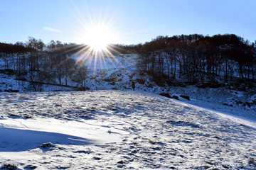 Winter landscape on a sunny day. Silhouette of a man against the background of a winter landscape. The bright sun sets over the hill on a winter day.