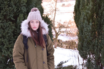 A beautiful girl is standing against a winter landscape. Close-up. The girl with the backpack has a thoughtful look.