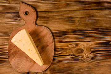 Cutting board with piece of cheese on wooden table. Top view