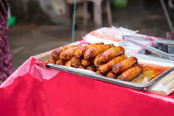 Traditional Thai charcoal roasted pork sausages in food tray on food market stall. Asian Thai street food, cuisine, gourmet, appetizer, fast and comfort food, starter, barbecue and grill meat concept