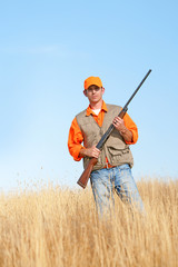 An adult male with a shotgun, wearing orange is hunting pheasant, quail, dove or chukkar.